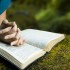 Young woman reading bible by stream in summer